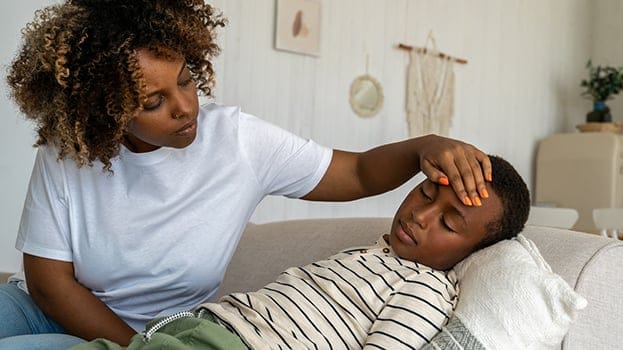Mother checking her sick child’s forehead at home, illustrating when families may need Arkansas Urgent Care services.
