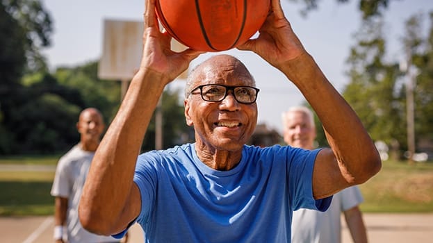 Older man playing basketball with two other men