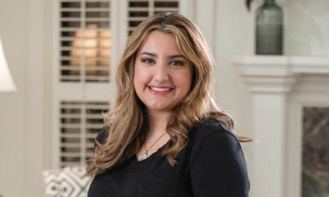 Woman smiling while seated indoors in a home setting.